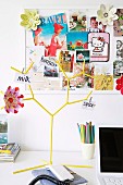 Postcards and flower decorations on pinboard behind yellow, tree-shaped rack with notes pegged to branches