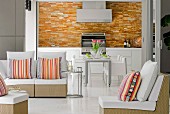 Mainly white designer furniture in living-dining room with splashes of colour provided by tiled kitchen wall and bright, striped cushions