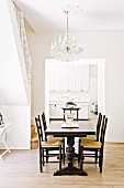 Dunkler Esstisch mit Stühlen in hellem Raum mit Kronleuchter und Durchgang zur weißen Küche