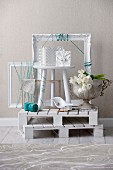 Stacked, white wooden pallets with white picture frames and large cup with white tulips