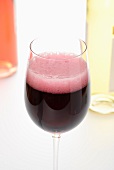 A glass of foaming red wine with white wine and rose wine in the background