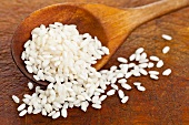 Raw short-grain rice on a wooden spoon and a wooden surface