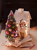 Paper house, porcelain figurine and artificial fir tree