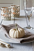 An autumnal place setting with an ornamental squash, tealight holders and a wine glass