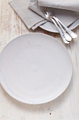 A simple white porcelain plate with forks and napkins next to it
