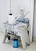 Runner of woven paper strips as centrepiece of shabby chic still-life with old metal watering can and vintage stool
