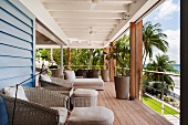 Überdachter Balkon mit bequemen Sitzmöbeln mit Blick auf Palmen und Strand