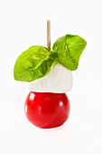 A tomato and mozzaella stick with basil against a white background