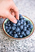 A woman taking a blueberry from a bowl