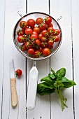Cherry tomatoes in a sieve with a bunch of fresh basil next to it