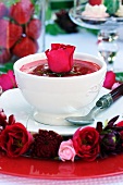 Strawberry soup with garnished with a red rose and a wreath of flowers decorating the plate