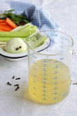 Chicken broth in a measuring jug, soup vegetables and cloves