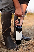 A woman opening a bottle of red wine in a field