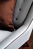 Silbergrauer Sessel im Ausschnitt mit kupferfarbenem Kissen