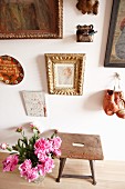 Pictures and boxing gloves on wall above old stool and bouquet of peonies