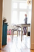 Postmoderne Acrylgas-Stühle und weisser Landhaustisch auf Dielenboden; Frau am Fenster
