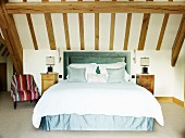 Elegantes Doppelbett mit grünblauer Husse und gepolstertem Kopfteil im Dachzimmer mit Holzbalkendecke