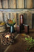 Small pine cone wreath, fern leaves, salt cellar and pepper mill on rustic wooden table