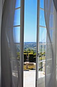 View of gardens and expansive landscape through open French windows with wafting curtains