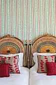Twin beds with elaborately carved and painted headboards against striped wallpaper