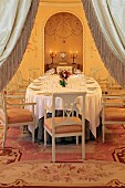 View through open curtains of festively set table in dining room with warm artificial lighting