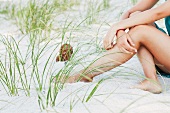 Teenage girl sitting on sandy beach amongst grasses