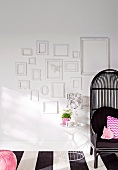 White picture frames on a white wall next to a black wicker chair