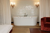 En suite bathroom separated by curtain with modern free-standing bathtub below antique sconces (Schloss Schauenstein)