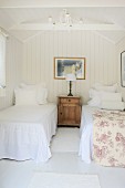 Bright, airy bedroom with antique bedside cabinet between twin beds