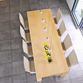 Blick von oben auf Esstisch aus Holz und Stühlen mit hellem Bezug auf hellgrauem Steinboden in minimalistischem Ambiente