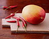 A mango and red chillis on a wooden board