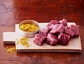 Diced lamb and curry powder on a wooden board