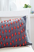 Grey cushion decorated with red pompom trim