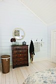 Antique chest of drawers and round mirror in wood-clad, attic bedroom