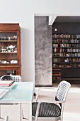 Moderner Designer-Essplatz und alter Geschirrschrank; im Hintergrund Blick auf Bücherwand mit Buchstabendeko