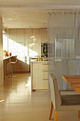Essbereich vor offener Küche mit Mittelblock und transparenter Vorhang als Sichtschutz