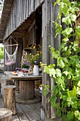 Holztisch mit Blumen und Baumstamm-Hocker auf der Terrasse einer Holzhütte