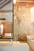 Designer Badezimmereinrichtung vor rustikaler Ziegelwand und Blick in Spiegel auf Bett
