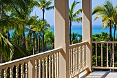 Veranda with white, carved wooden balustrade and sea view through palm trees