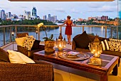 Lounge armchairs and lanterns on opium table on terrace with view of river and Brisbane skyline