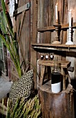 Still-life arrangement of cushions and decorative plants next to tree trunk table and bottle in front of glasses on wooden stool