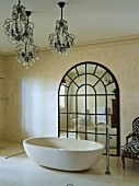 Freistehende Designer Badewanne mit Standarmatur und Kronleuchtern vor grossem Spiegel mit Rundbogen und Sprosseneinteilung in luxuriösem Bad