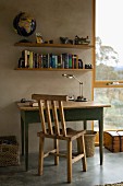Rustic wooden chair and table in front of a concrete wall and book shelves next to a floor to ceiling window with a view