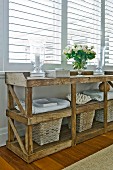 Rustikaler Holztisch mit Aufbewahrungskörben und frischer Wäsche; auf dem Tisch elegante Windlichter und ein weisser Sommerblumenstrauss