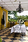 Dining area with delicate wrought iron furniture and wrought iron chandelier on a terrace with a diagonally laid checkerboard tile floor