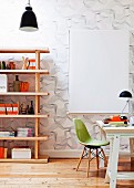 Desk and green shell chair next to modern wooden shelving against wallpaper with three dimensional pattern