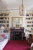 Violetter Teppich vor offenem Kamin zwischen Bücherregalen und Couch gegenüber Essplatz