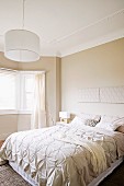 Doppelbett mit eleganter Tagesdecke und schlichte Hängeleuchte mit weißem Lampenschirm in beige getöntem Schlafzimmer mit traditionellem Flair