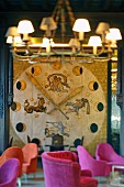 Enormous, floor-to-ceiling clock with phases of moon and zodiac applied to wall; armchairs with pink upholstery in foreground