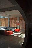 Puristische Hotellounge mit Strohmatten und leuchtroten Farbakzenten zum Grau von Sichtbeton und gradlinigen Sofas